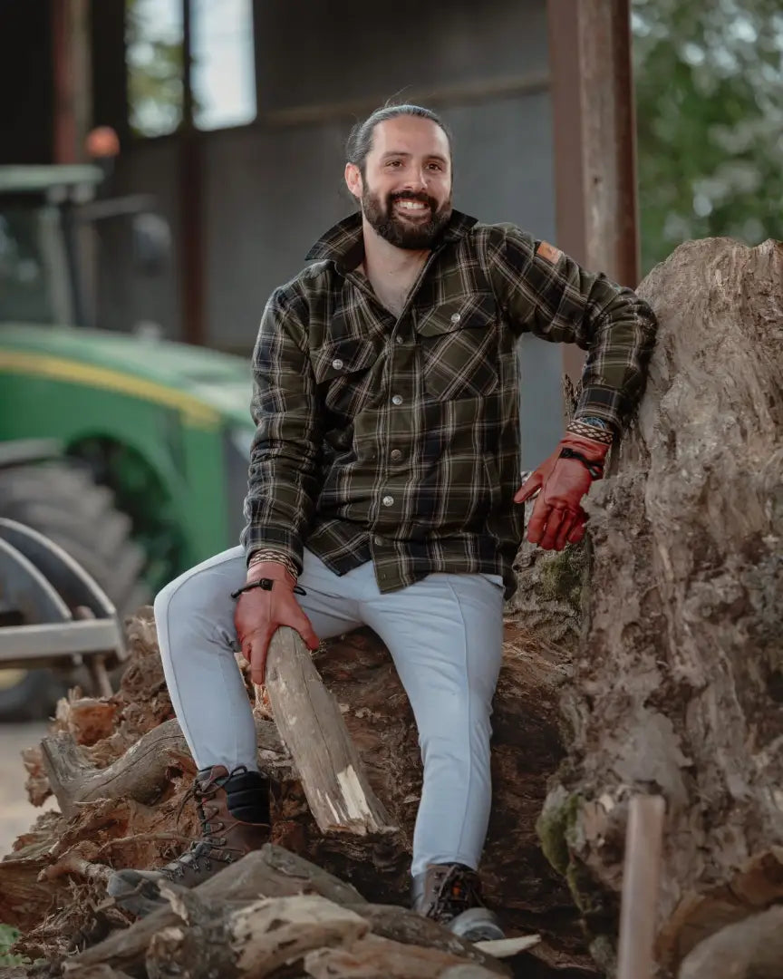 Man in plaid shirt sitting on wood showcasing the expertly made padded New Forest Padded Shirt