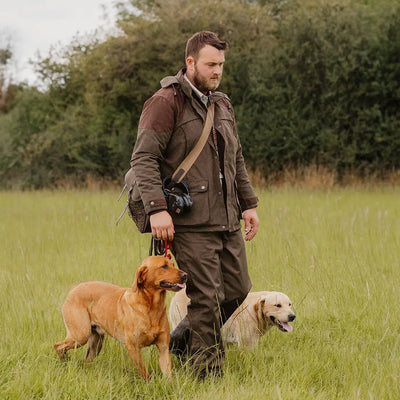 Man in New Forest Performance Field Coat walking two dogs in grassy field