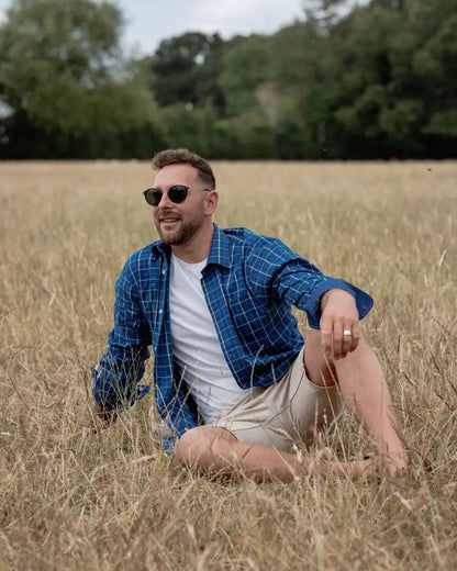 Man in sunglasses sitting in a field wearing the New Forest Premium Tattersall Shirt