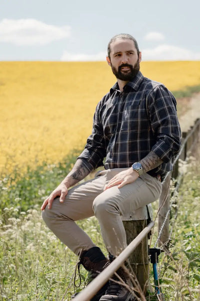 Man sitting on a fence in a forest premium tattersall shirt, stylish and comfy look