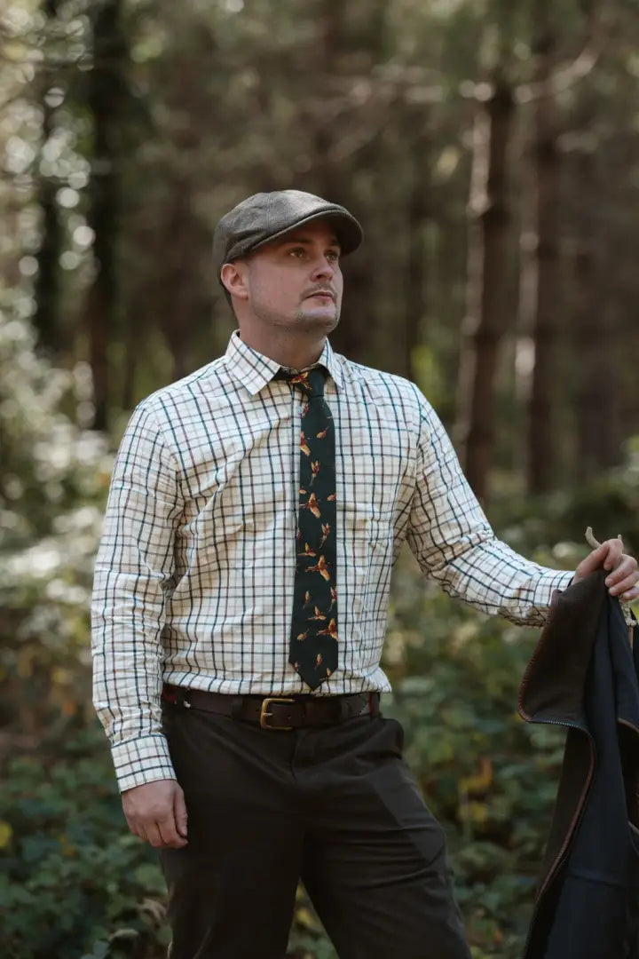 Man in forest premium tattersall shirt with dark tie and flat cap holding a jacket