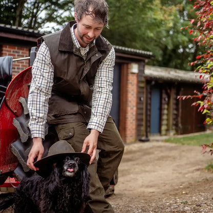 Man placing a hat on a black dog while wearing a New Forest Premium Tattersall Shirt
