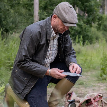 Man in flat cap and jacket examining hands, showcasing New Forest Premium Tattersall Shirt