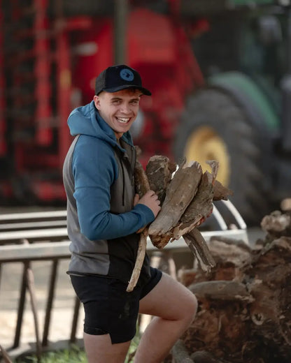 Smiling man wearing New Forest Raptor Hoodie carrying firewood in the forest