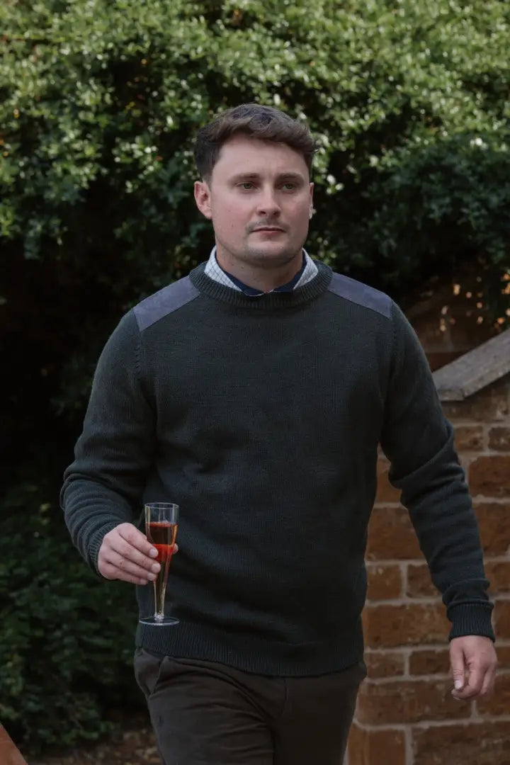 Man holding red wine wearing New Forest Raven Crew Neck Jumper in a cozy setting