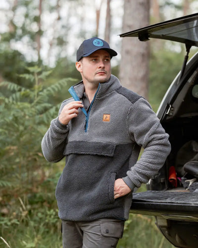 Man in gray fleece pullover wearing New Forest Trucker Hat showcasing rugged charm