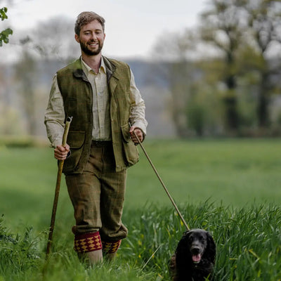 Man in countryside attire walks a black dog, showcasing New Forest Tweed Breeks with YKK zip