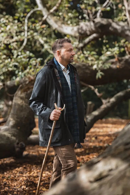 Man in Forest Woodsman Wax Jacket holding a wooden walking stick outdoors
