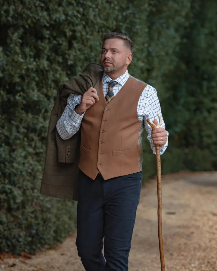 Man wearing forest wool mix waistcoat over checkered shirt with green jacket and walking stick