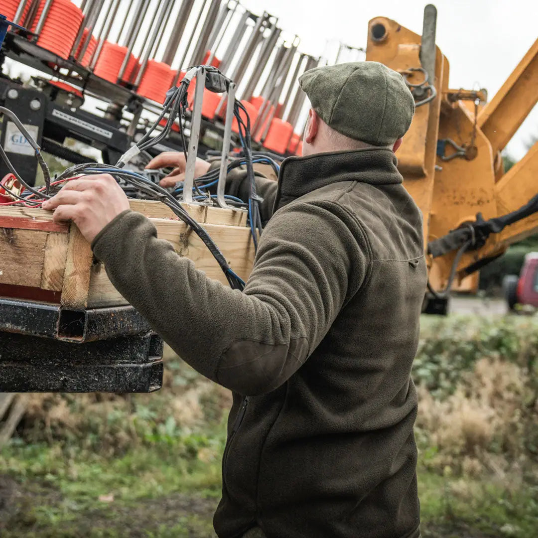 Man in green Fog Fleece Jacket working on machinery, perfect for country hunting gear