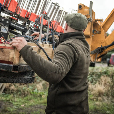 Man in green Fog Fleece Jacket working on machinery, perfect for country hunting gear