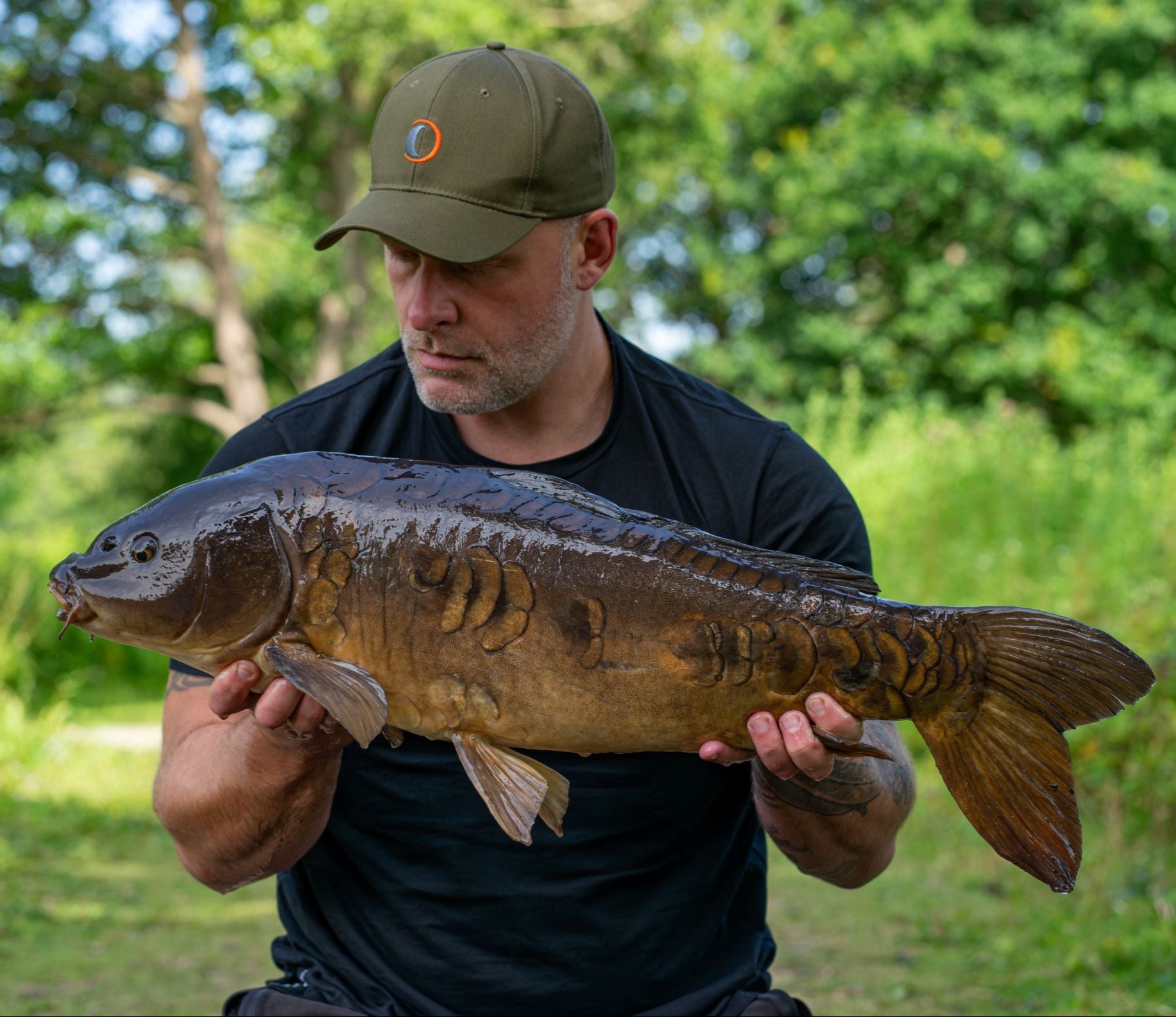 Man holding a large carp while wearing a Speero Baseball Cap for a stylish look