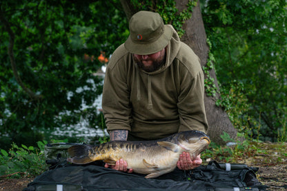 Man with a big carp wearing a Speero Reversible Bucket Hat for fishing adventures