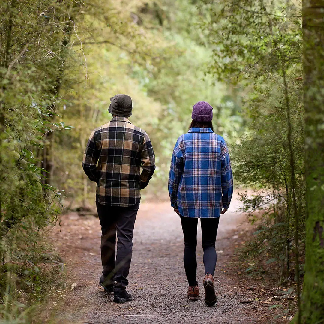 Two people in plaid shirts and hats walking on a wooded path wearing Swanndri Kiaraki v3 wool shacket