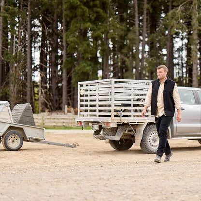 Man in Swanndri Saddleback Vest with khaki shirt walking outdoors next to pickup truck with stock crate in country clothing for hunting