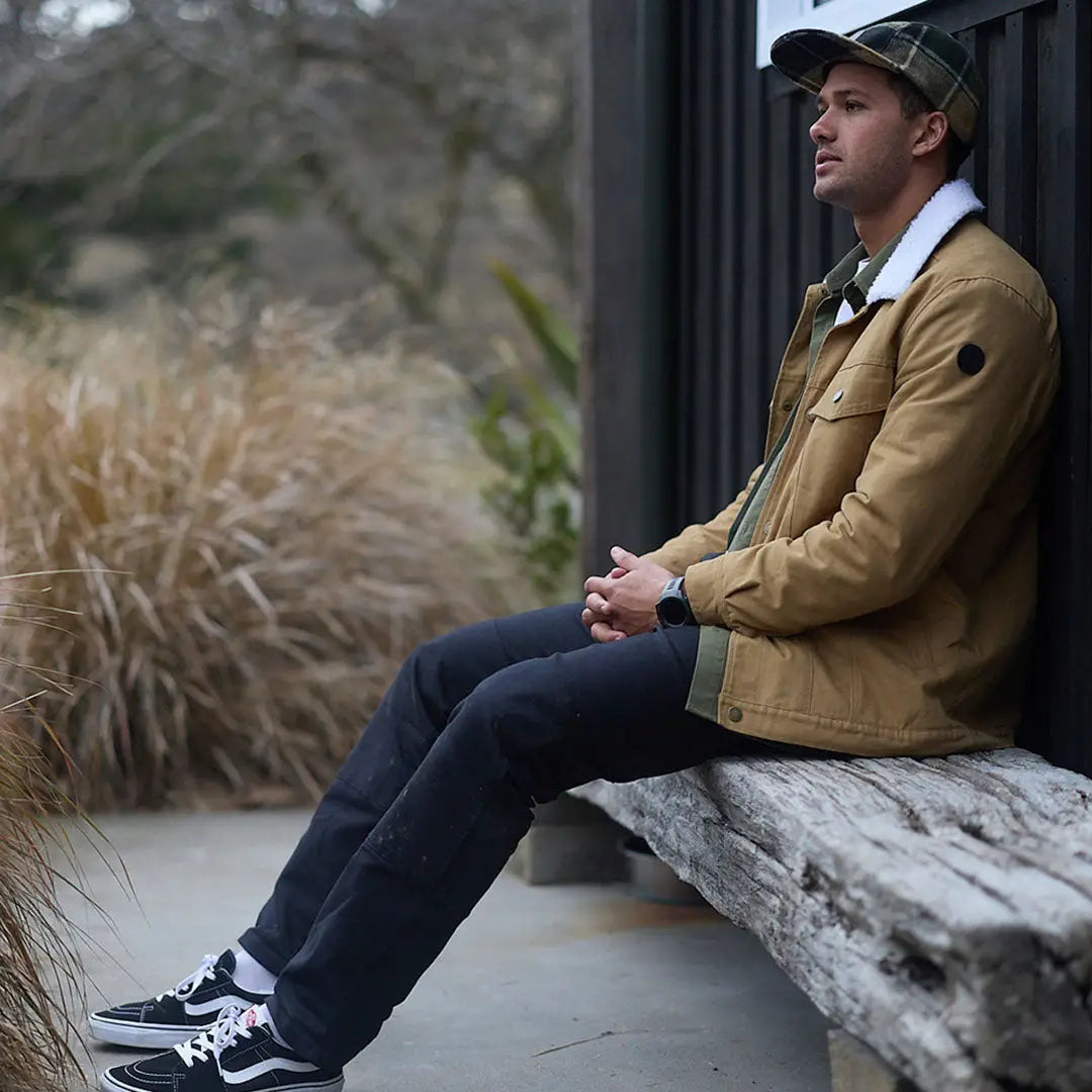 Man in tan jacket and dark jeans sitting on bench, showcasing Swanndri Wentworth Valley v2 Wool Cap