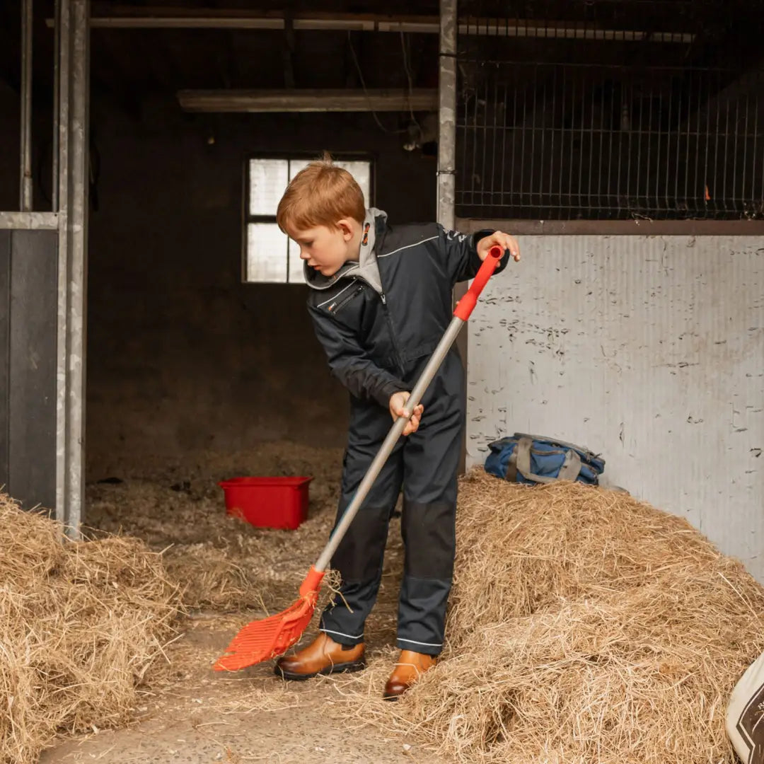 Young boy in Xpert Pro Junior Coverall sweeping hay in stable for protection and comfort