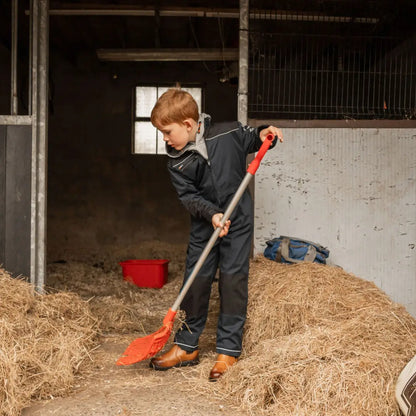 Young boy in Xpert Pro Junior Coverall sweeping hay in stable for protection and comfort